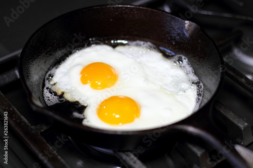 Two eggs frying sunny-side up in a cast iron pan on the stove.