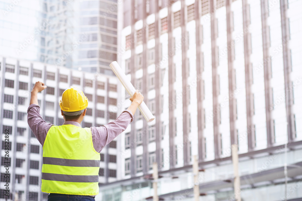 engineering man construction worker wear safety helmet for the safety of the work operation. engineer standing holding blueprint paper raised arms fist cheerful show project success. engineering man construction worker wear safety helmet for the safety of the work operation. engineer standing holding blueprint paper raised arms fist cheerful show project success.