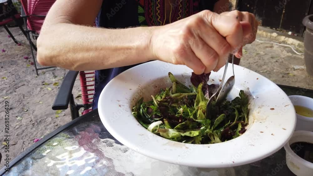 Closeup of mixed green salad at a cafe table with a woman dressed in colorful top. Closeup of mixed green salad at a cafe table with a woman dressed in colorful top.