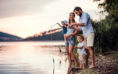 Young family with two toddler children outdoors by the river in summer, playing.
