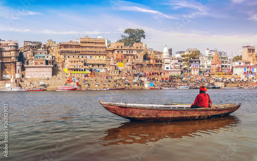Sadhu on a wooden boat on river Ganges with view of ancient Varanasi city architecture at sunset