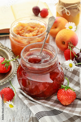 Jar of strawberry jam among summer and autumn fruits