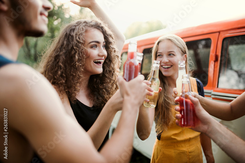 A group of friends standing outdoors on a roadtrip through countryside, clinking bottles. photo