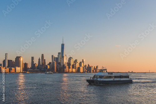 Boats traveling on Hudson River with skyline of lower Manhattan at sunset
