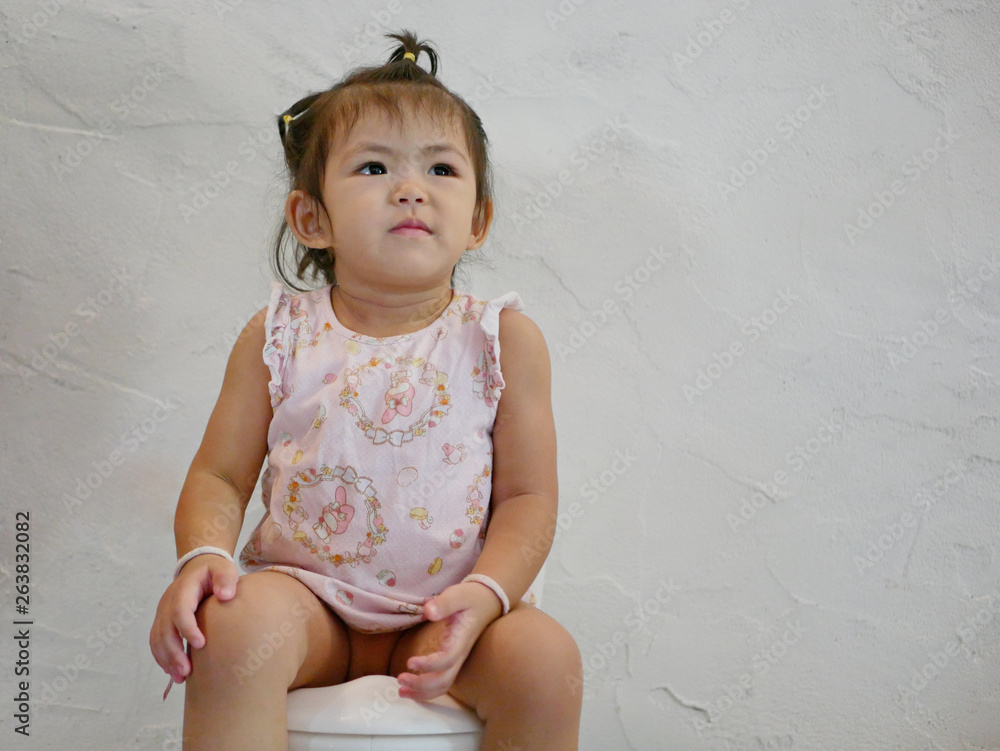 A 25 months old Asian baby girl sitting on a babysize toilet for a