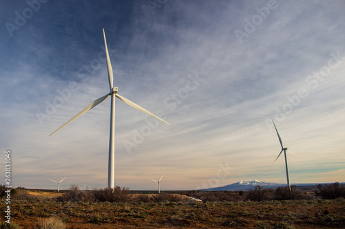 Wind turbines at a high elevation prairie landscape with mountains in the distance.