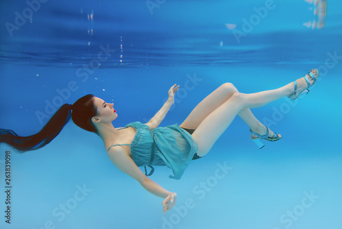 surreal, concept, art portrait of beautiful gorgeous brunette young woman with make up underwater in the swimming pool on blue background 