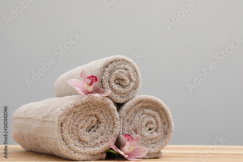 Stack of rolled towels and flowers on table. Space for text