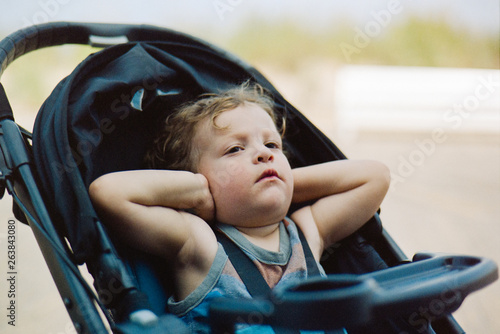 Toddler in stroller covering his ears photo