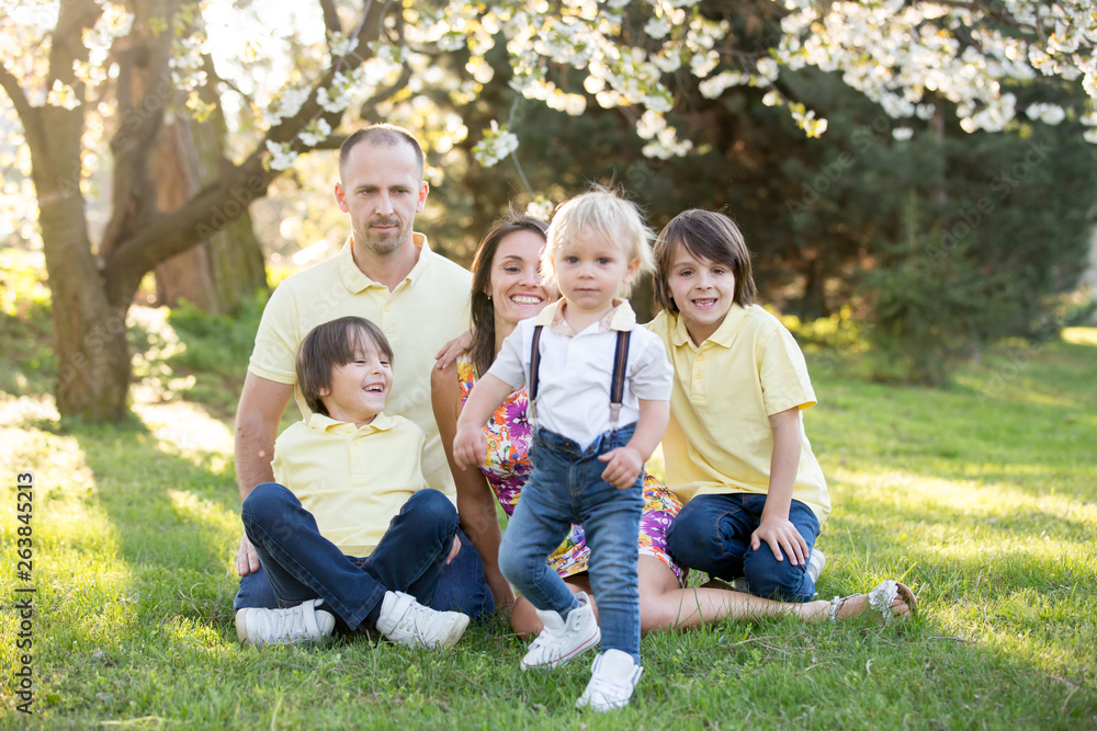 Beautiful family, mother, father and three kids, boys, having familly outdoors portrait taken on a sunny spring evening, beautiful blooming garden, sunset time Beautiful family, mother, father and three kids, boys, having familly outdoors portrait taken on a sunny spring evening, beautiful blooming garden, sunset time