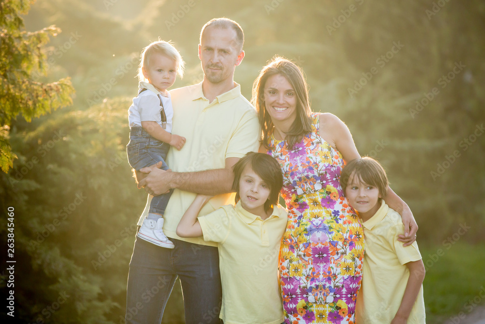 Beautiful family, mother, father and three kids, boys, having familly outdoors portrait taken on a sunny spring evening, beautiful blooming garden, sunset time Beautiful family, mother, father and three kids, boys, having familly outdoors portrait taken on a sunny spring evening, beautiful blooming garden, sunset time