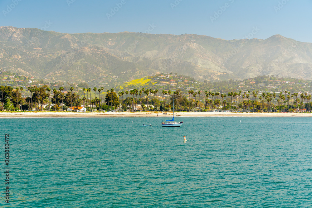 Obraz premium Santa Barbara Seashore o poranku. Łódź na wodzie, piękna plaża z palmami i góry na horyzoncie