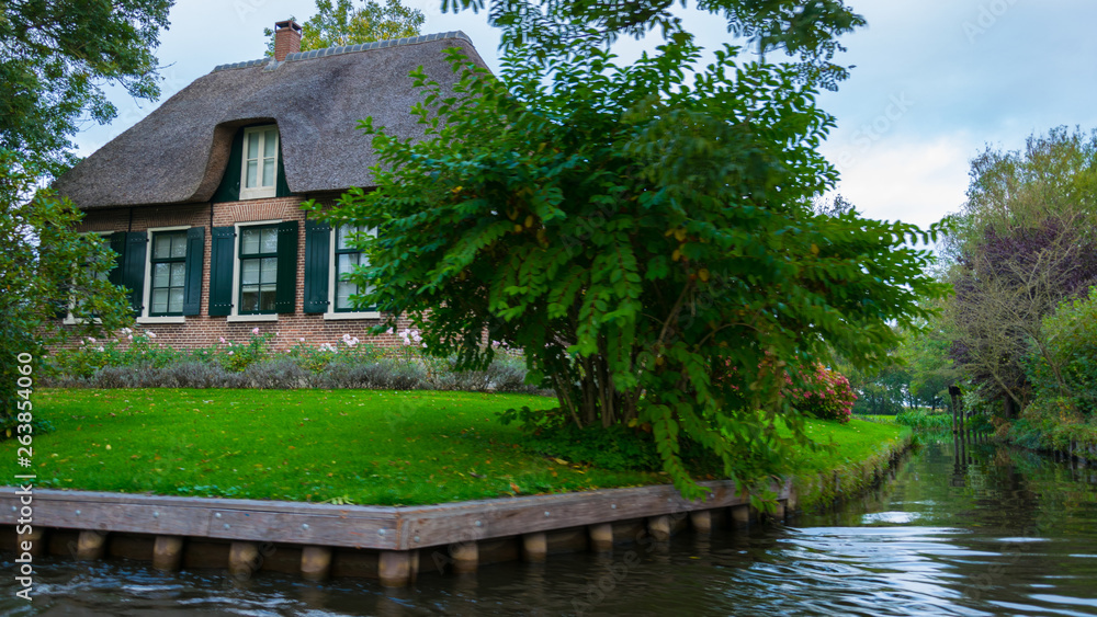 A house in Giethoorn, the Netherlands, photographed on water channels on a fall day, with green grass, and special architecture of the area. A house in Giethoorn, the Netherlands, photographed on water channels on a fall day, with green grass, and special architecture of the area.