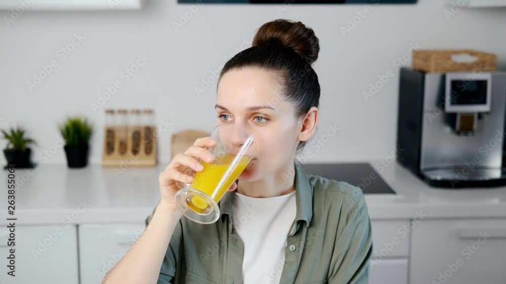 Young brunette woman drinking orange juice in the kitchen, close-up Young brunette woman drinking orange juice in the kitchen, close-up