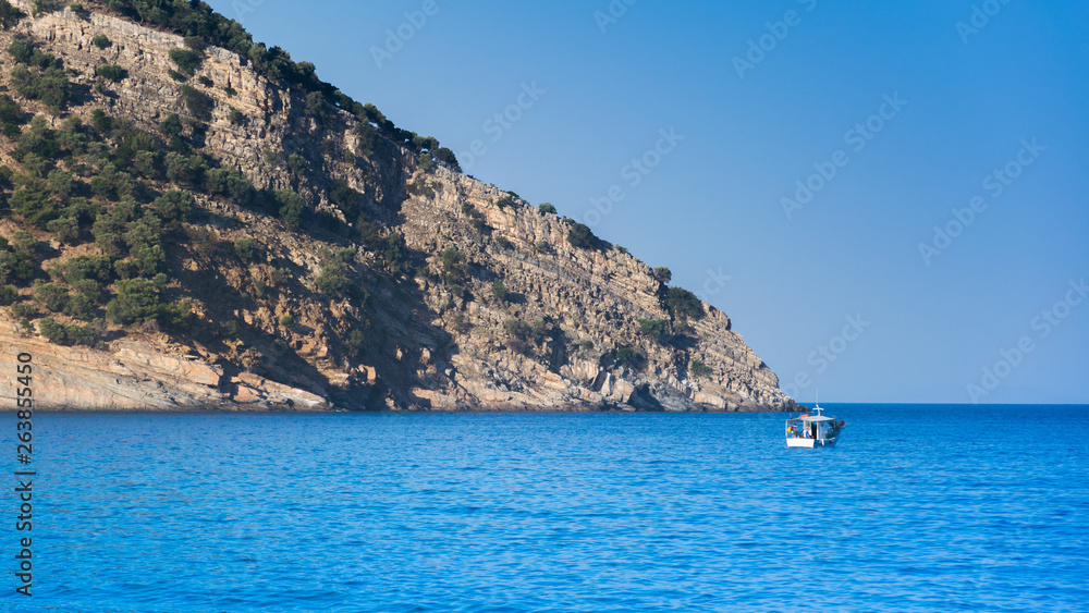 an island with trees in the Mediterranean Sea and a boat on the blue sea