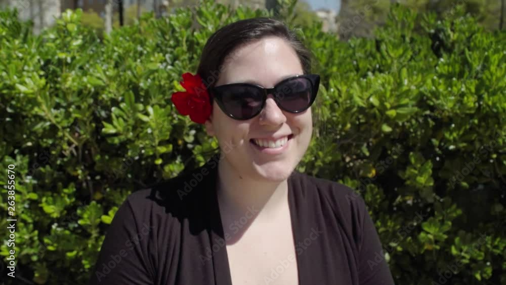 Smiling woman fixing hair with red flower in breeze and looking to side, Slowmo Smiling woman fixing hair with red flower in breeze and looking to side, Slowmo