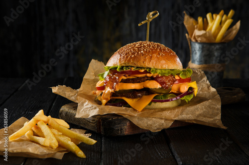 Cheeseburger and french fries on wooden table on dark background.