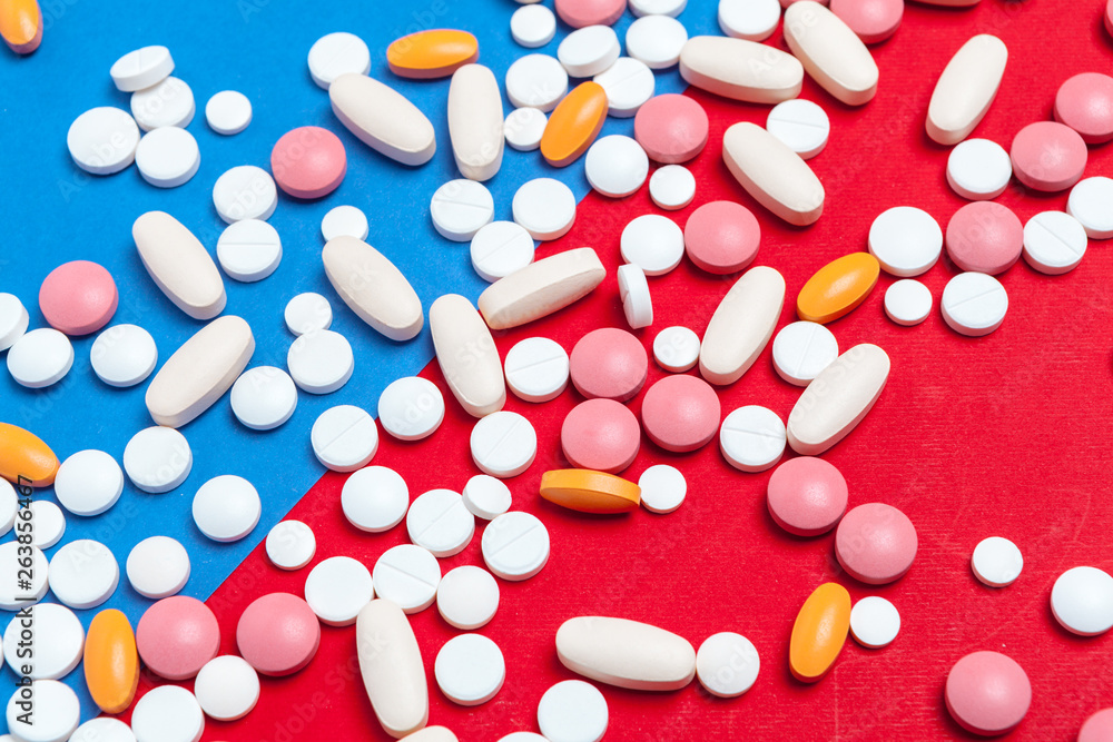 Multicolored pills on blue and red background. Medical concept. Texture. Multicolored pills on blue and red background. Medical concept. Texture.