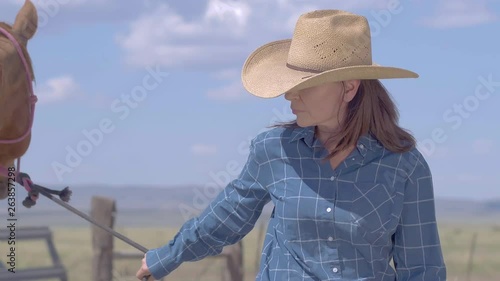 Female rancher looking over farm while leading beautiful brown horse by bridle 4k photo