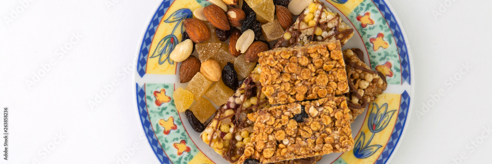 vegan dessert: several cereal bars with raisins and honey are on a bright plate, a lot of nuts and candied fruits are lying around, short focus vegan dessert: several cereal bars with raisins and honey are on a bright plate, a lot of nuts and candied fruits are lying around, short focus