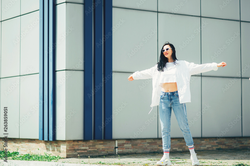 Hipster girl wearing blank white t-shirt, jeans and sunglasses posing  against rough street wall, minimalist urban clothing style. Freedom  lifestyle fashion concept Stock Photo | Adobe Stock