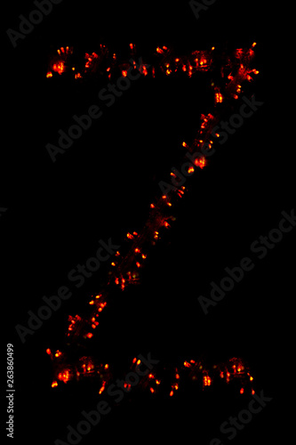 The letter "Z" of the English alphabet made of red electric garland on a dark background, blur, bokeh, isolated on black