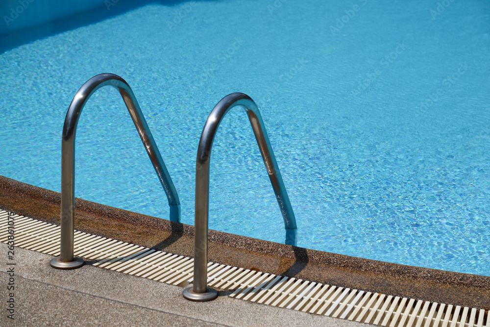 Closeup of stainless ladder of outdoor swimming pool with clear blue water.