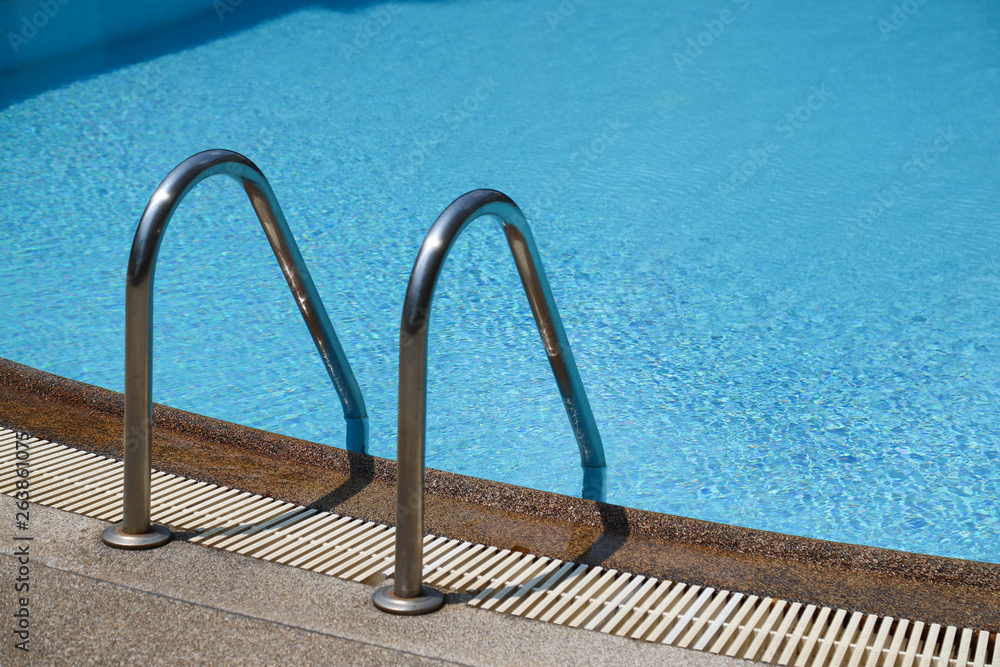 Closeup of stainless ladder of outdoor swimming pool with clear blue water. Closeup of stainless ladder of outdoor swimming pool with clear blue water.