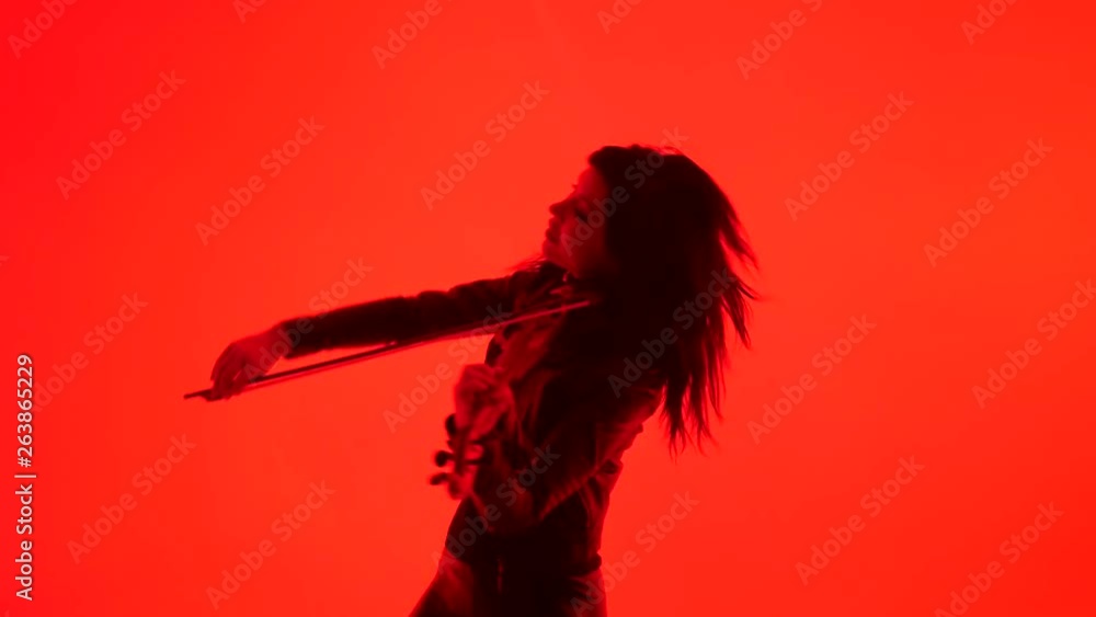 slim sensual young Asian girl in tight black leather clothes expressively plays the electric violin on a red background slim sensual young Asian girl in tight black leather clothes expressively plays the electric violin on a red background