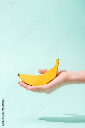 cropped view of young woman holding paper banana on turquoise with copy space
