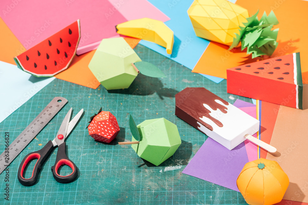 Naklejka origami fruits and colorful cardboard with scissors and ruler on messy surface
