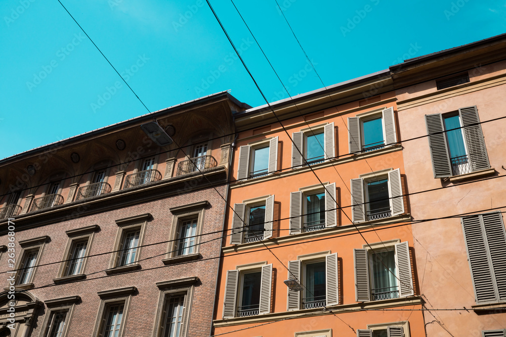 orange, pink apartment with windows, shutters, balcony in Bologna, Italy. Against blue sky