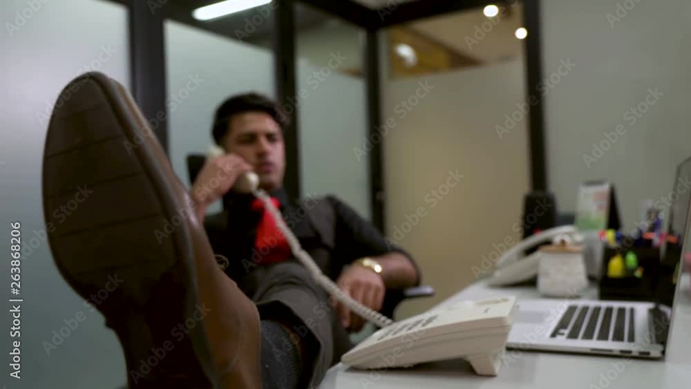 Business man working in his office, put his feet on the desk relaxing while talking on the phone. Business man working in his office, put his feet on the desk relaxing while talking on the phone.