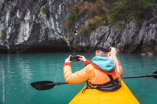 The girl takes a picture of a beautiful landscape sitting in a kayak.. kayaking tour of the islands, a holiday in Asia, a kayak's nose on the water. photograps in the boat photo