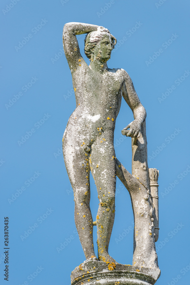 Ancient statue covered with moss and lichen of a naked hunter in Potsdam, Germany