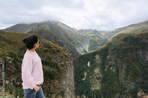 young girl in a sweater is looking at the Caucasian mountains, Georgia, rear view. copy space