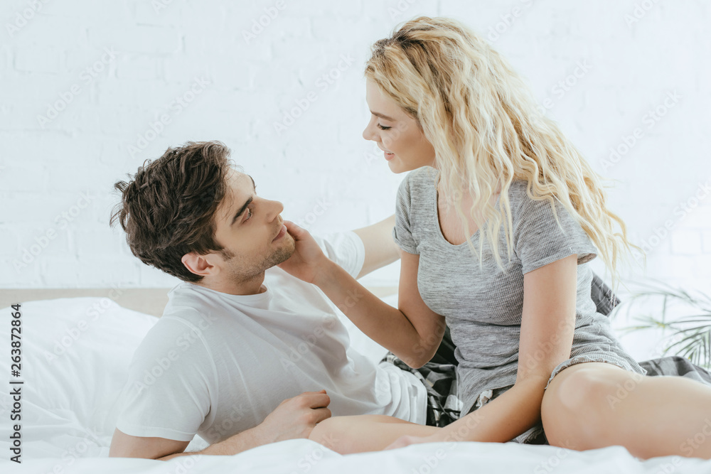 happy blonde woman touching cheek of handsome man lying on bed happy blonde woman touching cheek of handsome man lying on bed