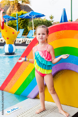 The child is going to jump and dive into the pool. . Colorful rainbow swimwear for little kids. Little girl having fun on a family summer vacation at the resort. Beaches water activities