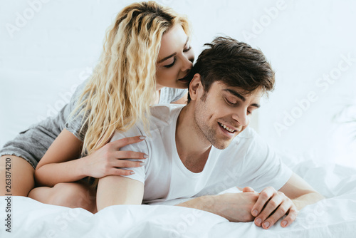 beautiful blonde girl hugging handsome boyfriend lying on bed
