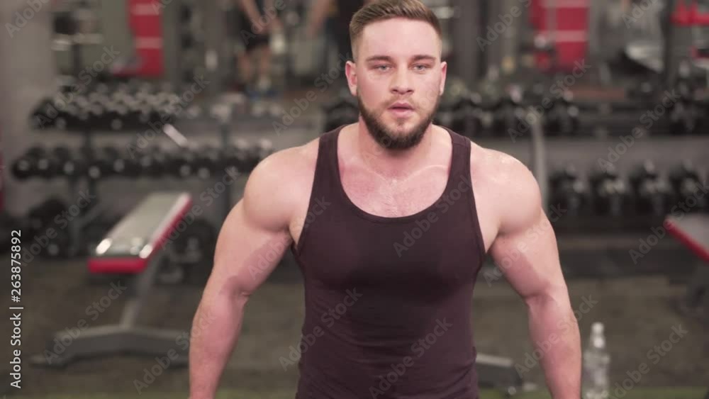 Caucasian Male Bodybuilder Taking to Somebody on Break and Starts Again With Biceps Exercise on Cable Machine in Gym. Blurred Background Caucasian Male Bodybuilder Taking to Somebody on Break and Starts Again With Biceps Exercise on Cable Machine in Gym. Blurred Background