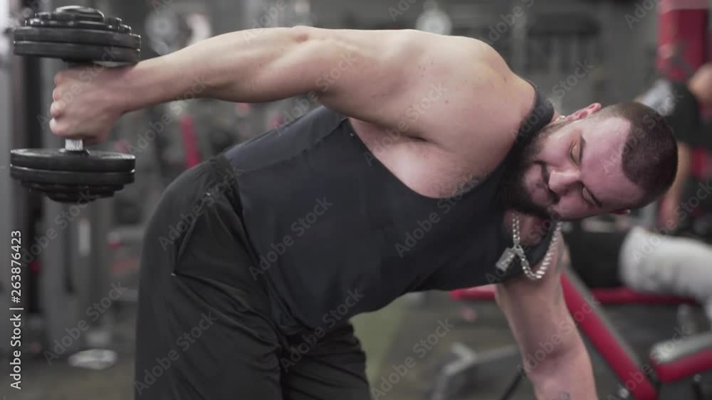 Strong Caucasian Male Bodybuilder Working Out in Gym on His Hands Muscles With Weights. Light Camera Movement and Blurred Background Strong Caucasian Male Bodybuilder Working Out in Gym on His Hands Muscles With Weights. Light Camera Movement and Blurred Background