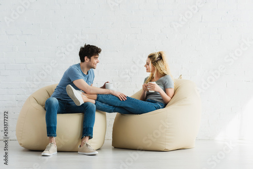 cheerful woman and happy man sitting on bean bag chairs and holding cups