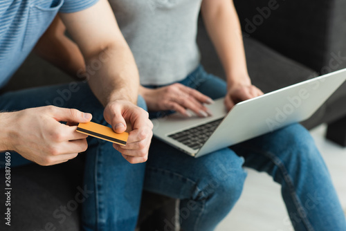 cropped view of man holding credit card near young woman using laptop