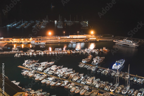 Aerial view of boats and beautiful city at night in Sorrento, Italy. Amazing landscape with boats in marina bay, sea, city lights, mountains, Harbor with yacht
