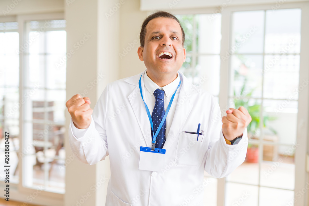 Middle age doctor man wearing medical coat and id card badge over white background celebrating surprised and amazed for success with arms raised and open eyes. Winner concept.