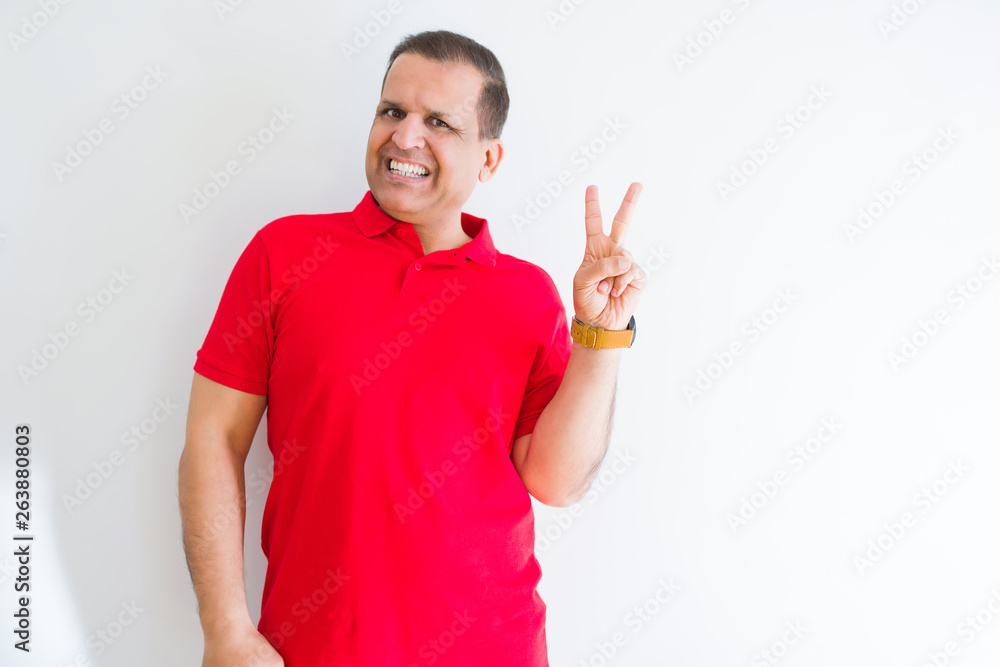 Middle age man wearing red t-shirt over white wall smiling with happy face winking at the camera doing victory sign. Number two. Middle age man wearing red t-shirt over white wall smiling with happy face winking at the camera doing victory sign. Number two.