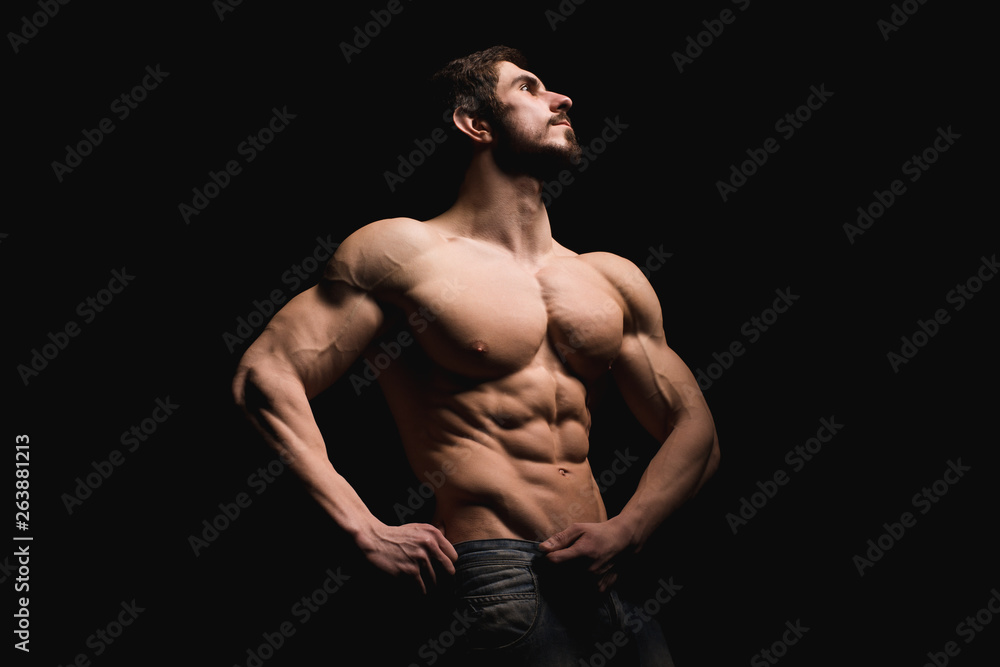 Portrait of shirtless muscular man in a jeans. Young male hunk showing his perfect body and muscles on black background.