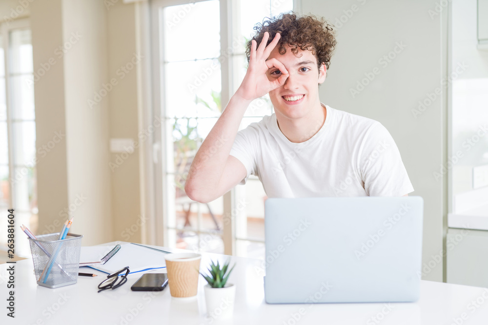 Young student man working and studying using computer laptop with happy face smiling doing ok sign with hand on eye looking through fingers