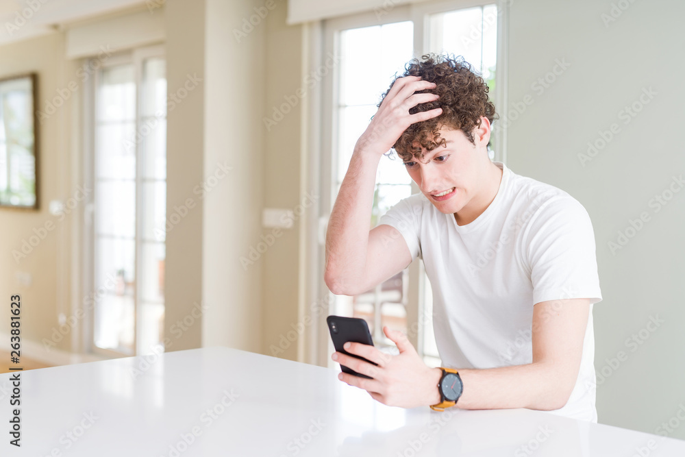 Young man using smartphone at home stressed with hand on head, shocked with shame and surprise face, angry and frustrated. Fear and upset for mistake. Young man using smartphone at home stressed with hand on head, shocked with shame and surprise face, angry and frustrated. Fear and upset for mistake.