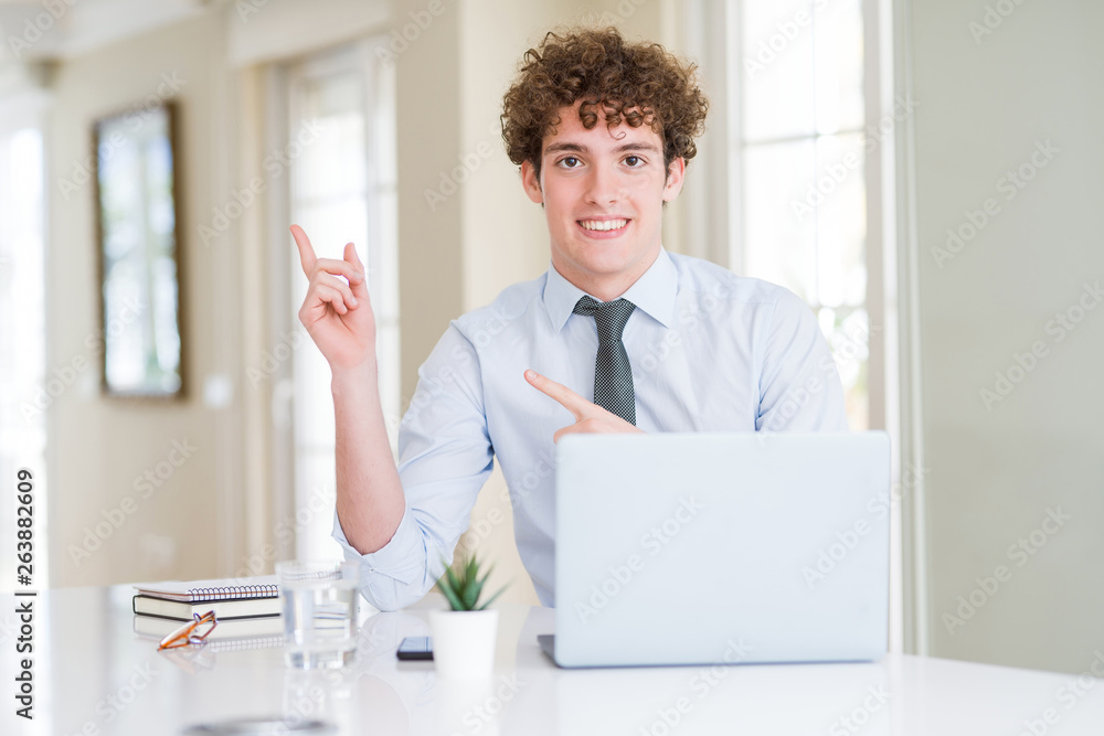 Young business man working with computer laptop at the office smiling and looking at the camera pointing with two hands and fingers to the side.